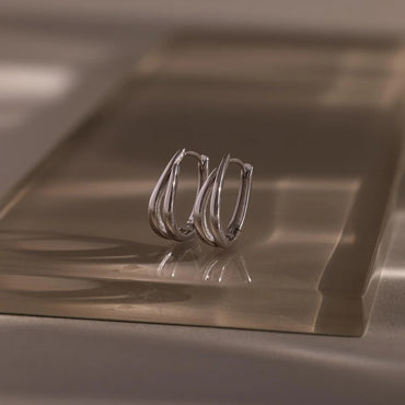 Pair of silver hoop earrings on a reflective metallic surface