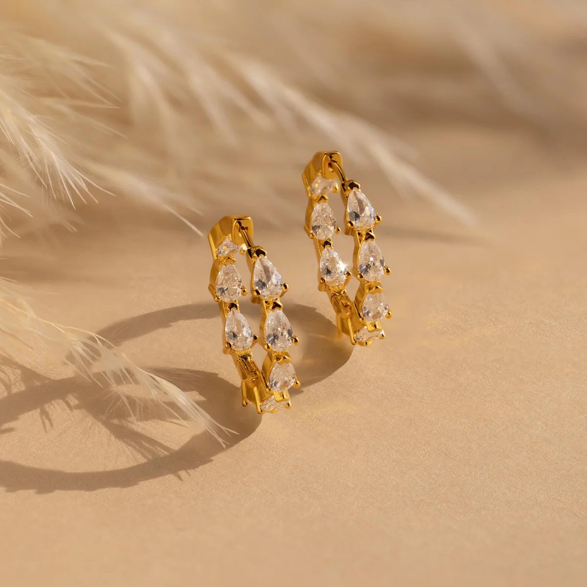 Gold hoop earrings with clear stones on a beige background