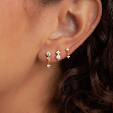 Close-up of an ear wearing gold and diamond earrings with a blurred background