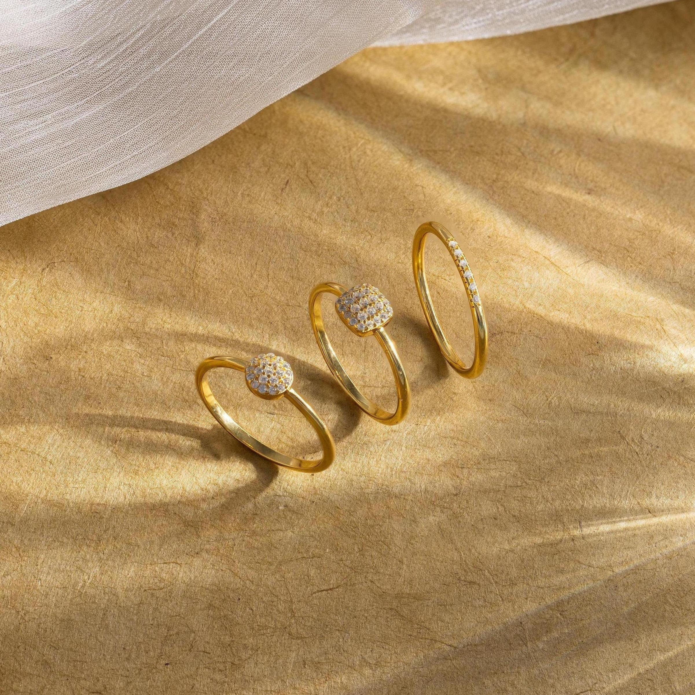 Three gold rings with gemstones on a beige fabric background