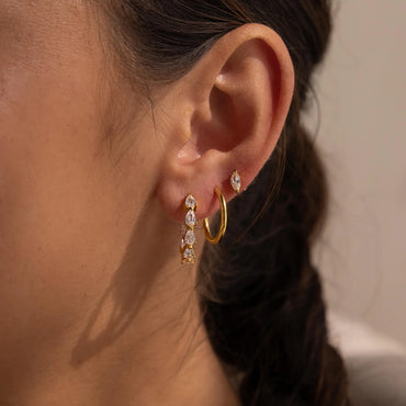 Close-up of an ear wearing gold hoop earrings with clear gemstones.