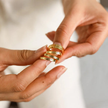 Gold rings being held between fingers with a neutral background
