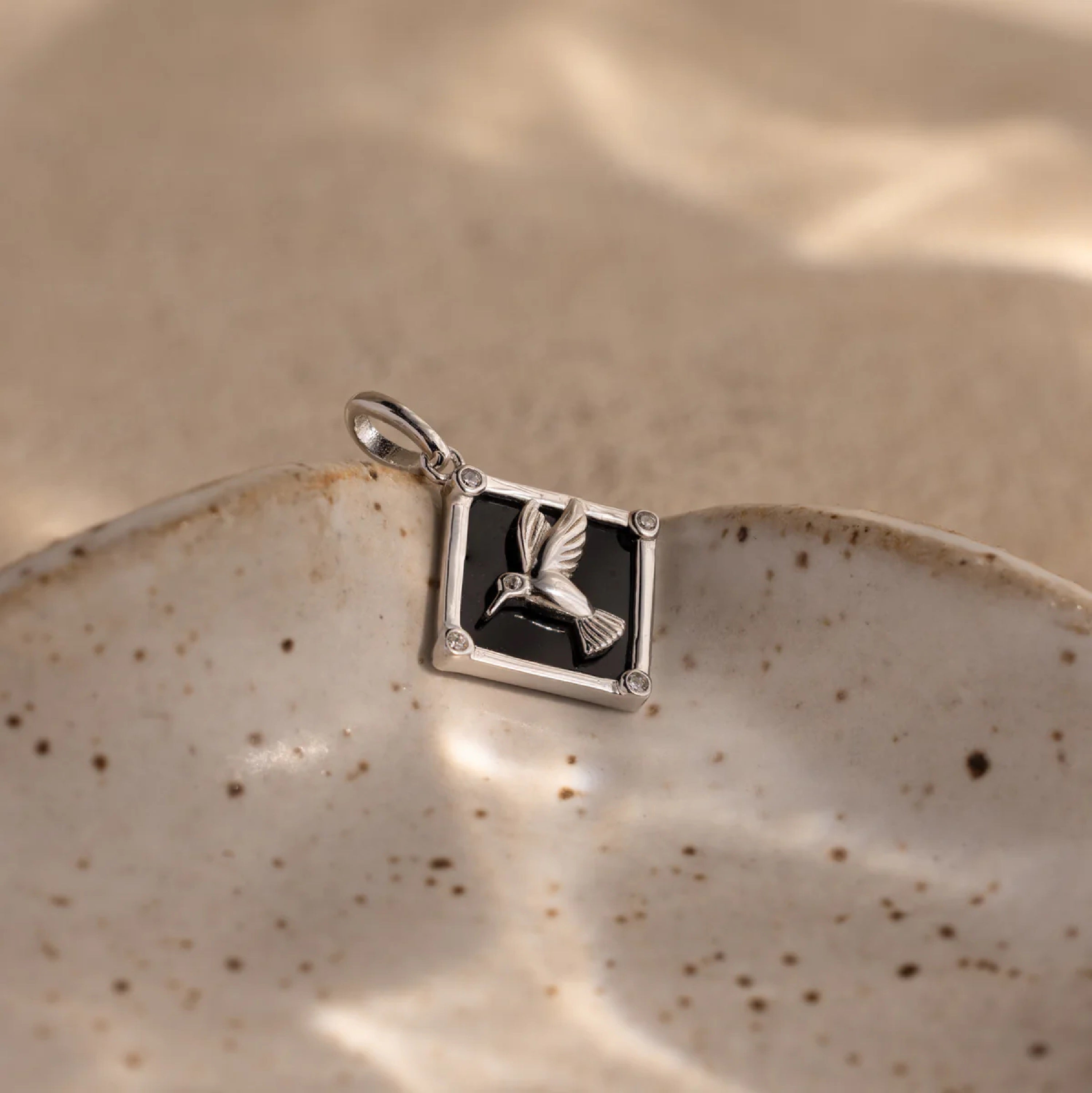 Silver pendant with a black stone and bird design on a ceramic plate