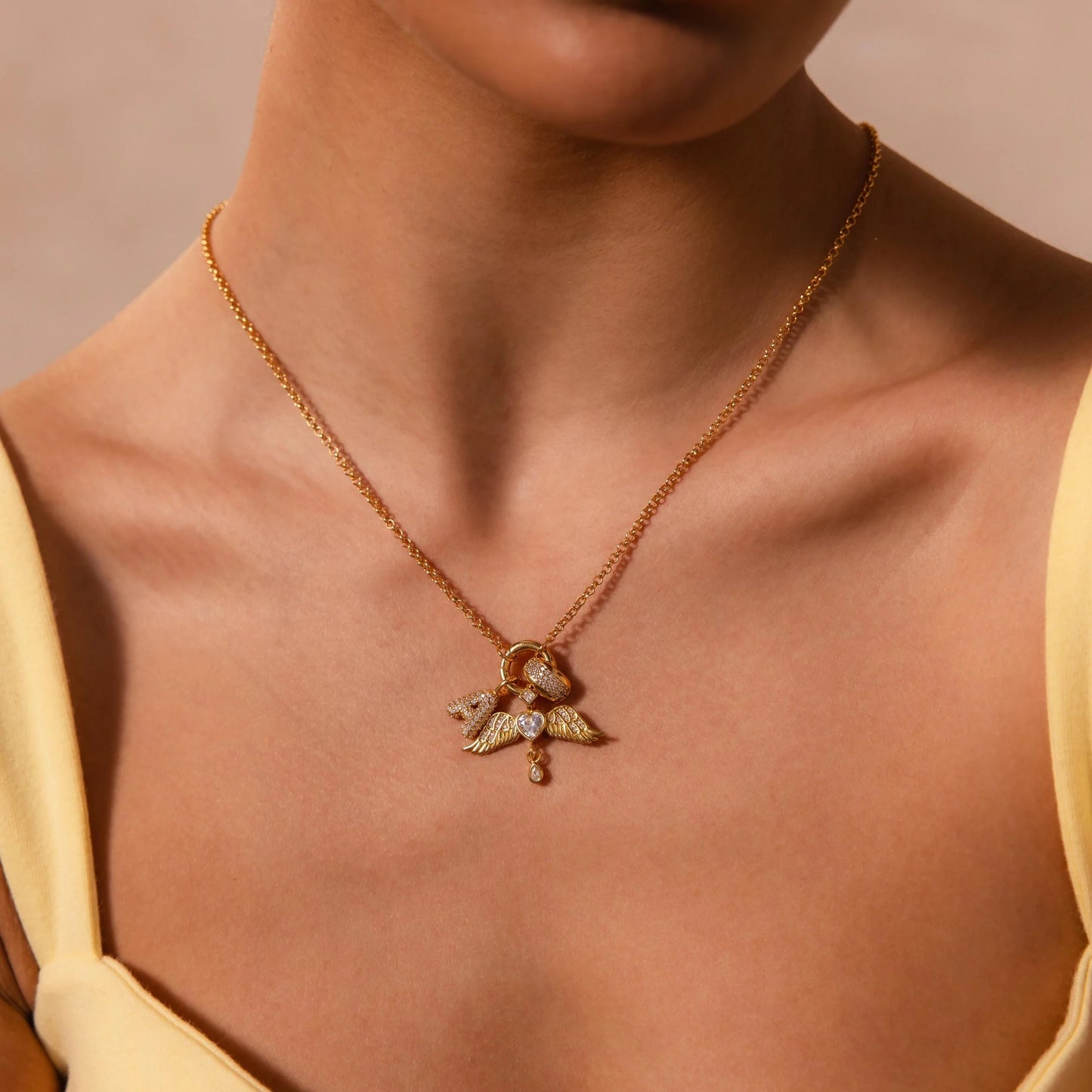 Gold necklace with a pendant on a person wearing a yellow top against a beige background