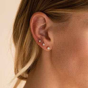 A close-up image of a woman's ear wearing a gold Booker Diamond Stud with a round cut CZ diamond.