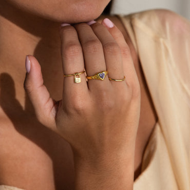 A person wearing a gold initial padlock ring on their finger.