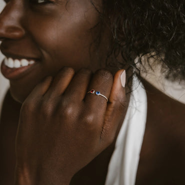 A close-up image of a person's hand featuring a Dual Birthstone Ring with two blue stones on the finger.