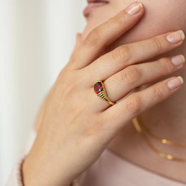 A close-up image of a woman's hand showcasing a vintage-inspired garnet signet ring with a gold finish.
