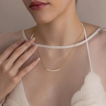 A model wearing a dainty pearl curve necklace with a fine cable chain, showcased on a white, delicate outfit.
