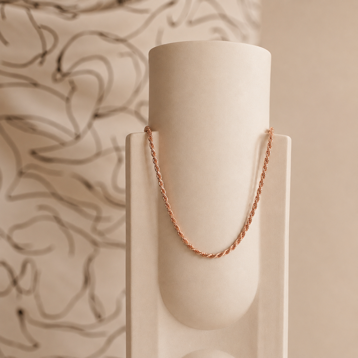 Rose gold chain on a white cylindrical stand against a beige background