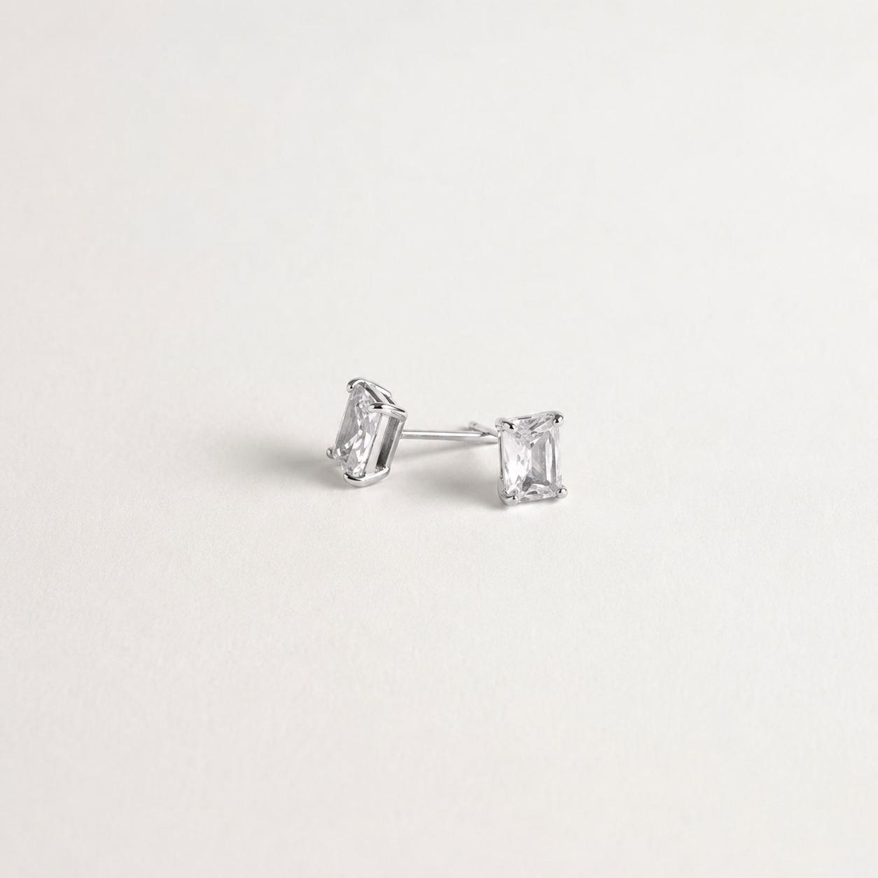A pair of silver stud earrings with rectangular clear gemstones, displayed on a clean, light off-white background.
