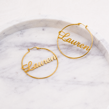 Gold hoop earrings with 'Lauren' engraved on a marble surface