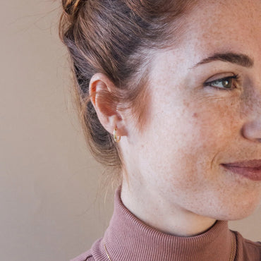 A person wearing Kaia Diamond Huggie Earrings with small, evenly spaced sparkling CZ stones around a sleek hoop, in silver or gold finish.