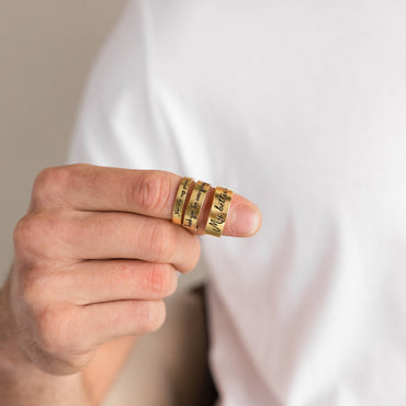 A close-up image of a hand wearing a gold band ring with custom handwriting engraved on it.