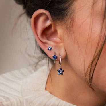 A person wearing a pair of blue sapphire flower earrings with silver accents.