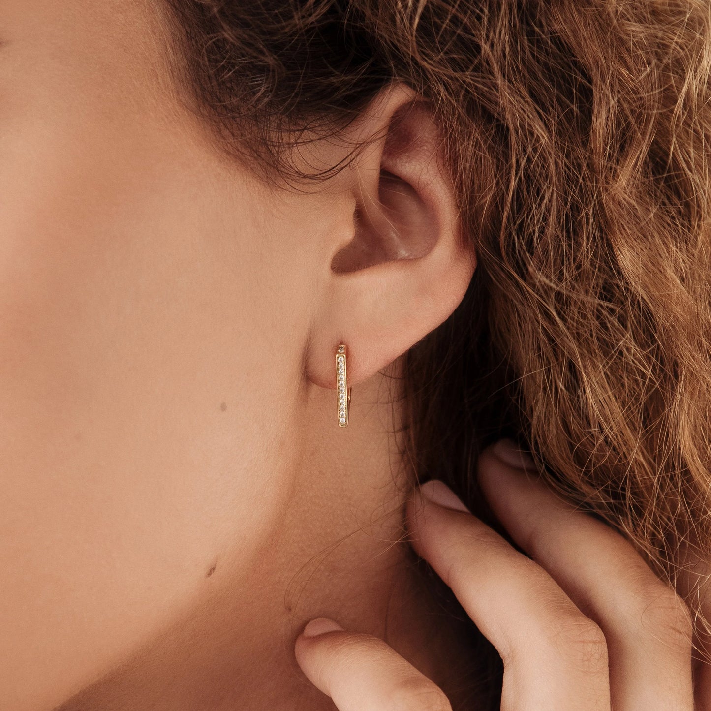 A person wearing a hoop earring with a geometric pave design.