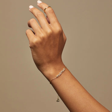 A hand wearing a silver bracelet with the word 'mama' in cursive letters, adorned with small round diamonds.