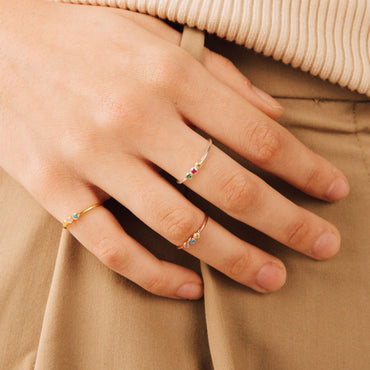 A person's hand showcasing a dainty ring with three colorful stones on the finger.