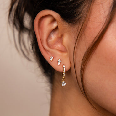 A close-up image of a woman's ear wearing a gold drop earring with a diamond design.