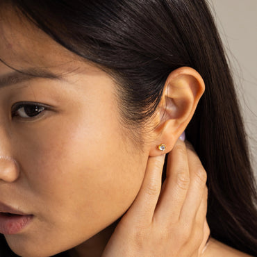 A close-up image of a woman's ear wearing a silver stud earring with a moonstone gemstone.