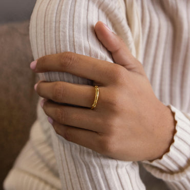 A close-up image of a person's hand wearing a dainty gold-colored ring with a beaded design on a finger.