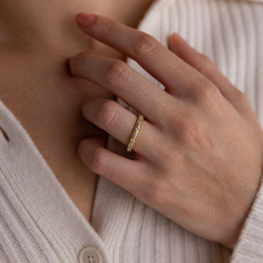 A close-up image of a person's hand wearing a gold-coated diamond eternity ring with a beaded band and pavé CZ diamond gemstones.