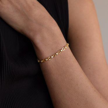A person wearing a black outfit showcasing a gold tennis bracelet with diamond-like gemstones on their wrist.