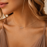 Close-up of a woman wearing a gold necklace with 'Demi' pendant against a neutral background