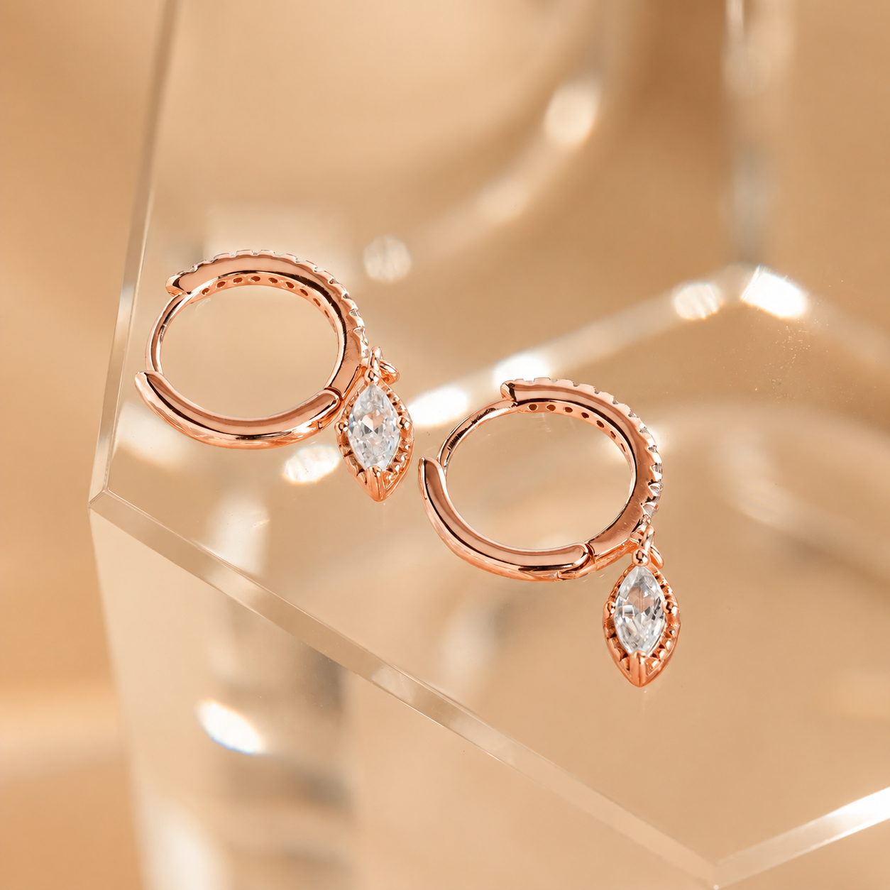 Rose gold hoop earrings with teardrop-shaped gemstones on a reflective surface.