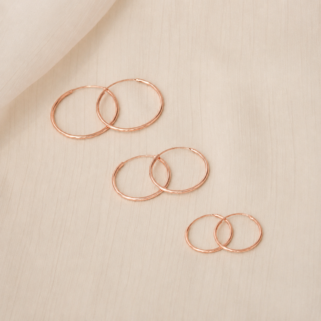 Set of rose gold hoop earrings on a beige fabric background