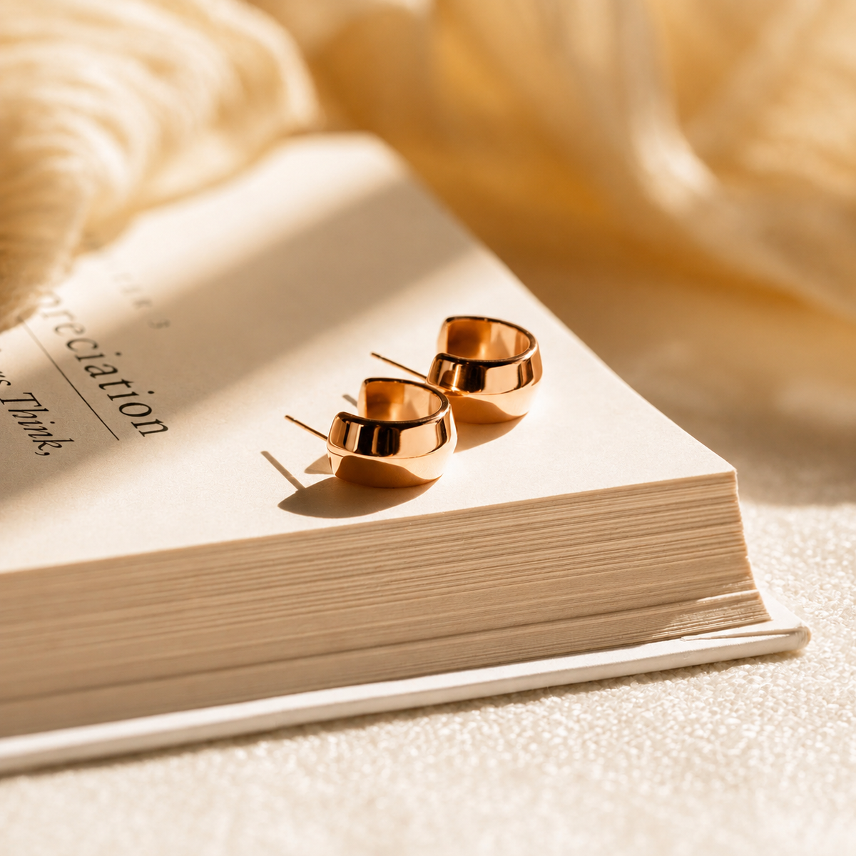 Rose gold hoop earrings on an open book with soft focus background
