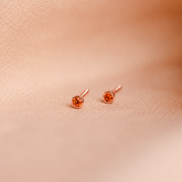 Rose gold earrings with orange gemstones on a soft pink fabric background