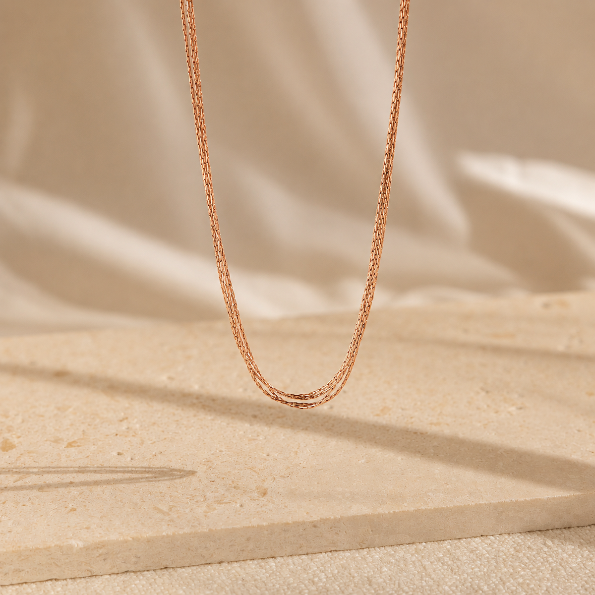 Rose gold chain necklace on a beige fabric background