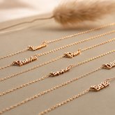 Set of gold necklaces with engraved names on a neutral background