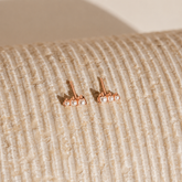 Rose gold earrings with pearls on a textured beige surface