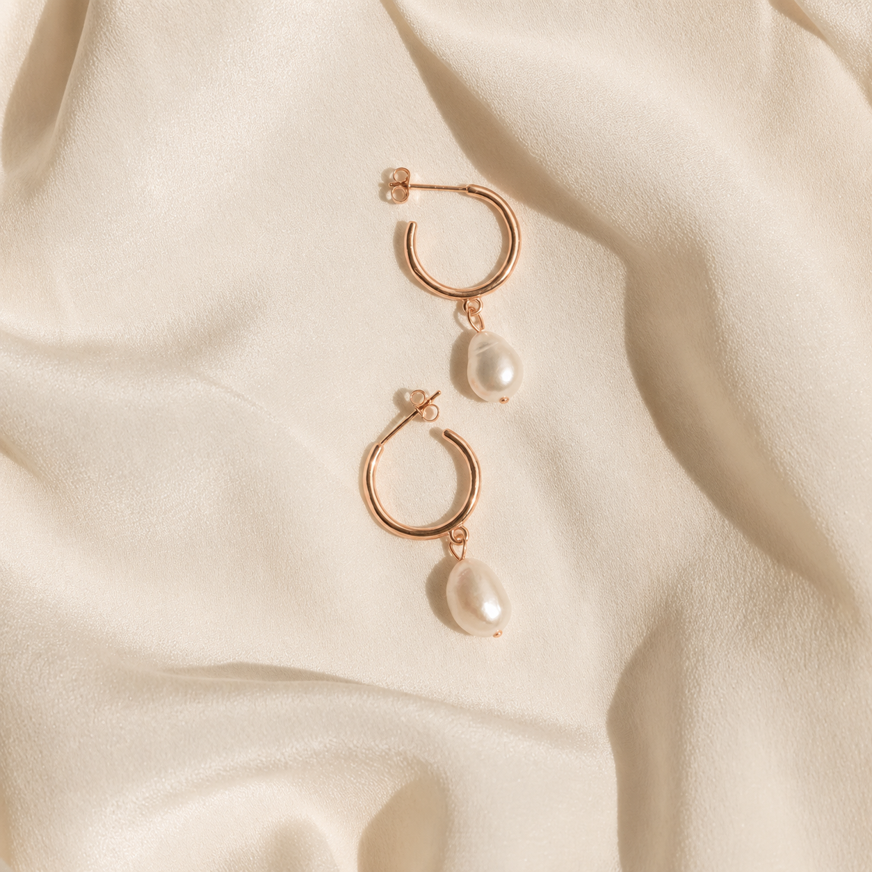 Rose gold hoop earrings with pearls on a beige fabric background