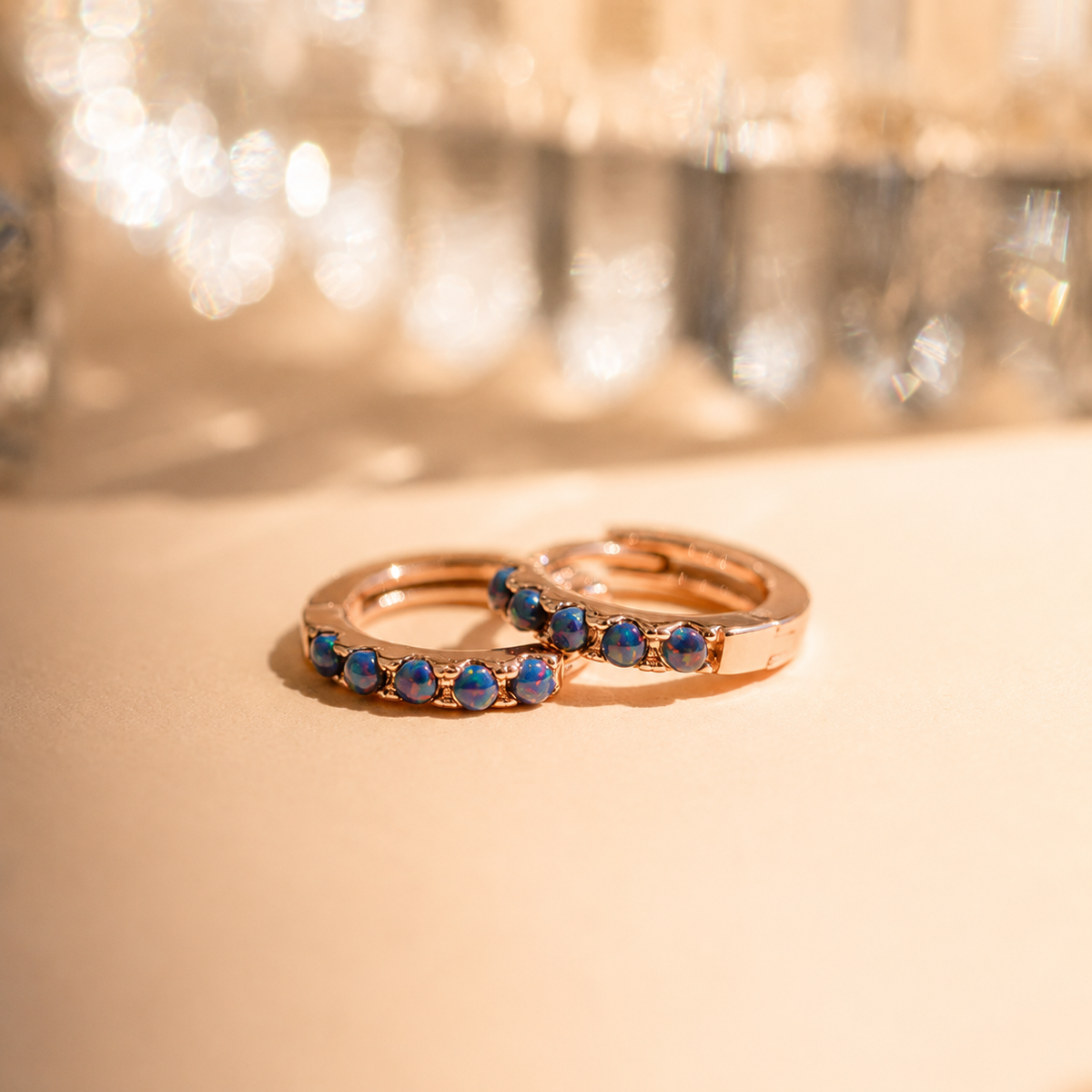 Two rose gold rings with blue gemstones on a beige surface