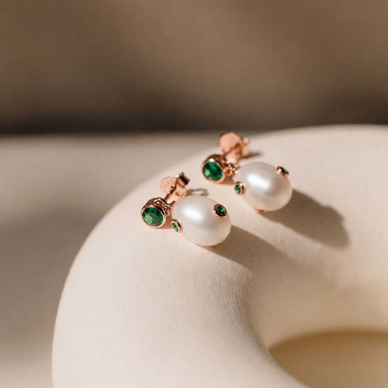 Pearl earrings with green gemstones on a beige background
