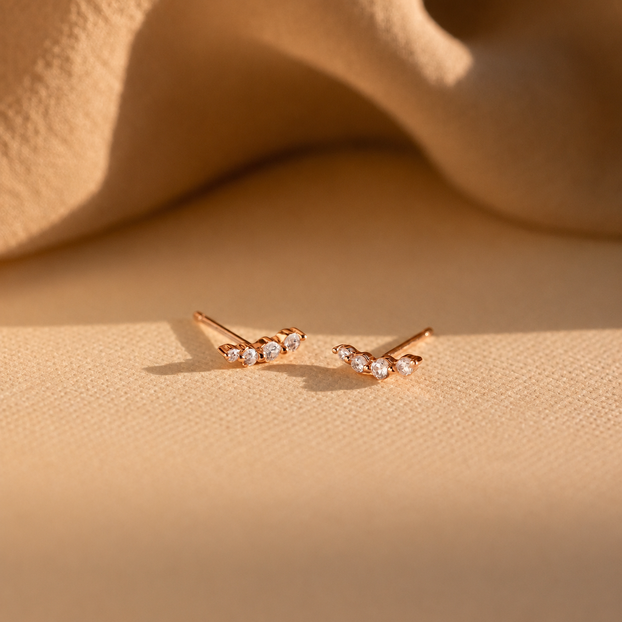 Rose gold earrings with small diamonds on a beige surface