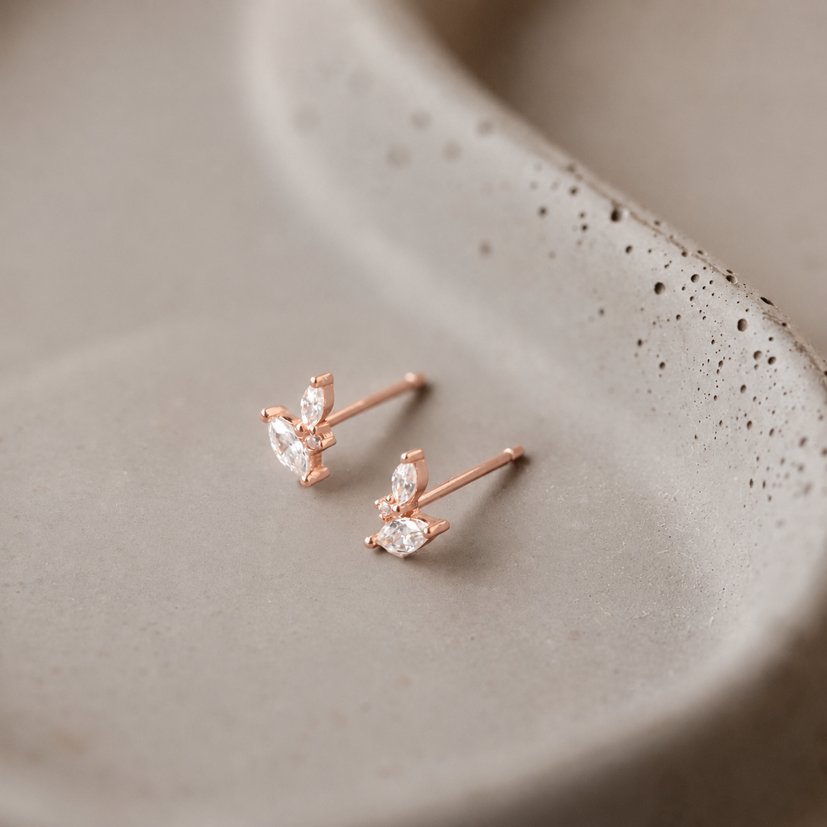 Rose gold earrings with clear gemstones on a textured beige surface