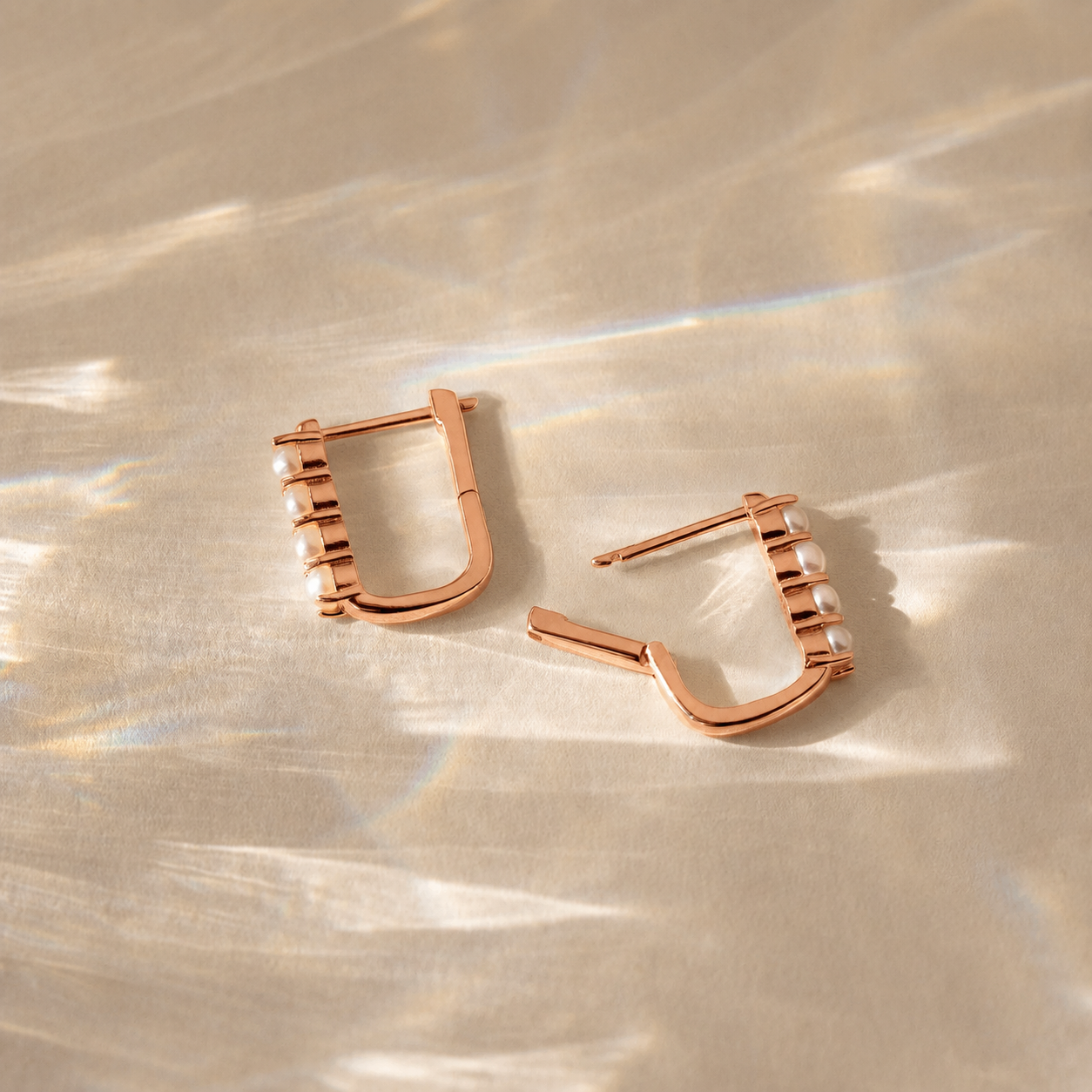 Rose gold hoop earrings on a textured beige surface