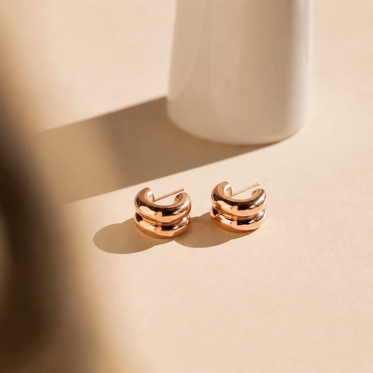 Rose gold earrings on a beige surface with soft shadows