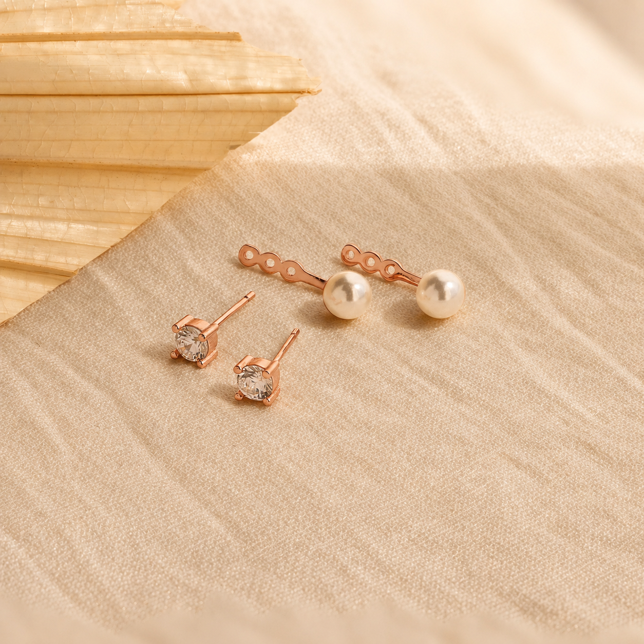 Pair of rose gold earrings with clear gemstones on a beige fabric background