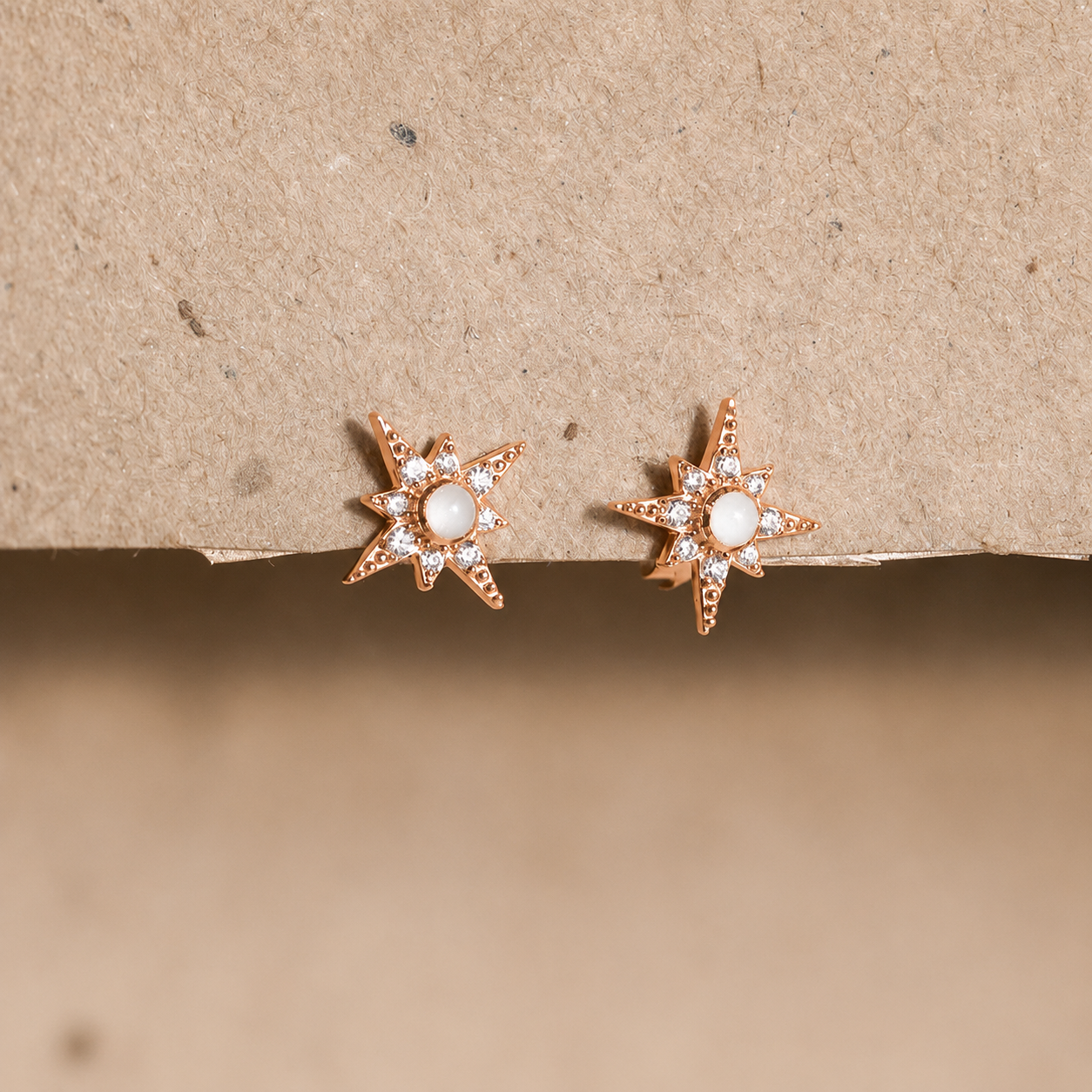 Star-shaped earrings with a central gemstone on a beige background
