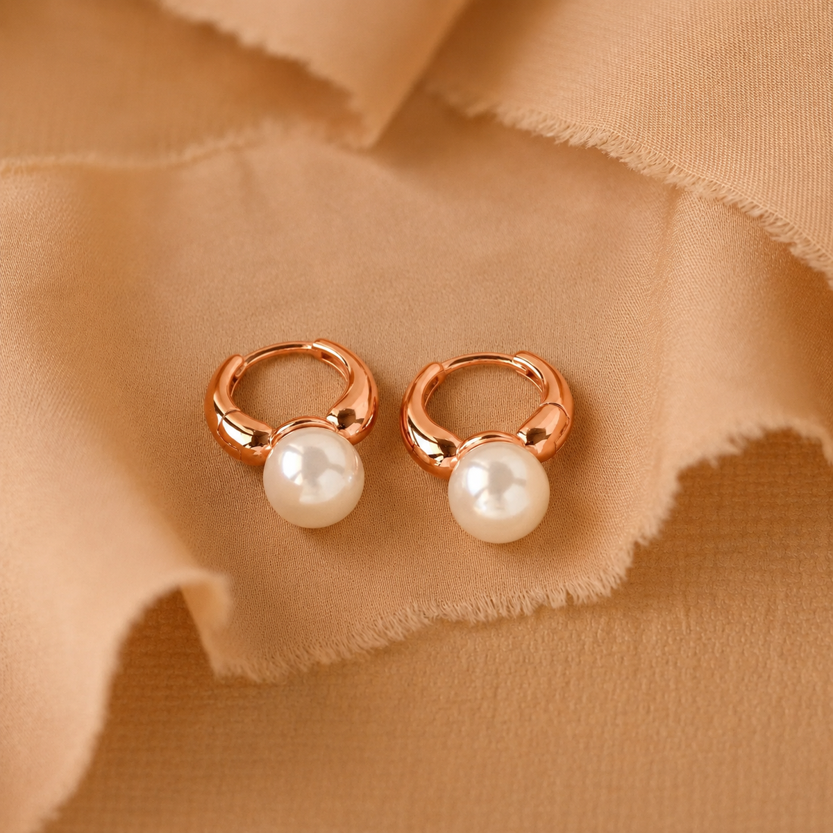 Rose gold hoop earrings with pearls on a beige fabric background