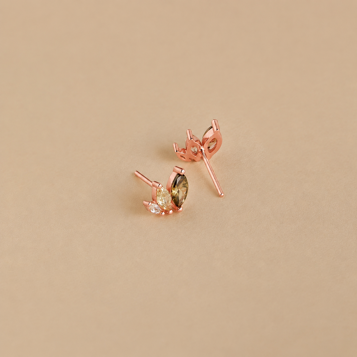 Rose gold earrings with green gemstones on a beige background
