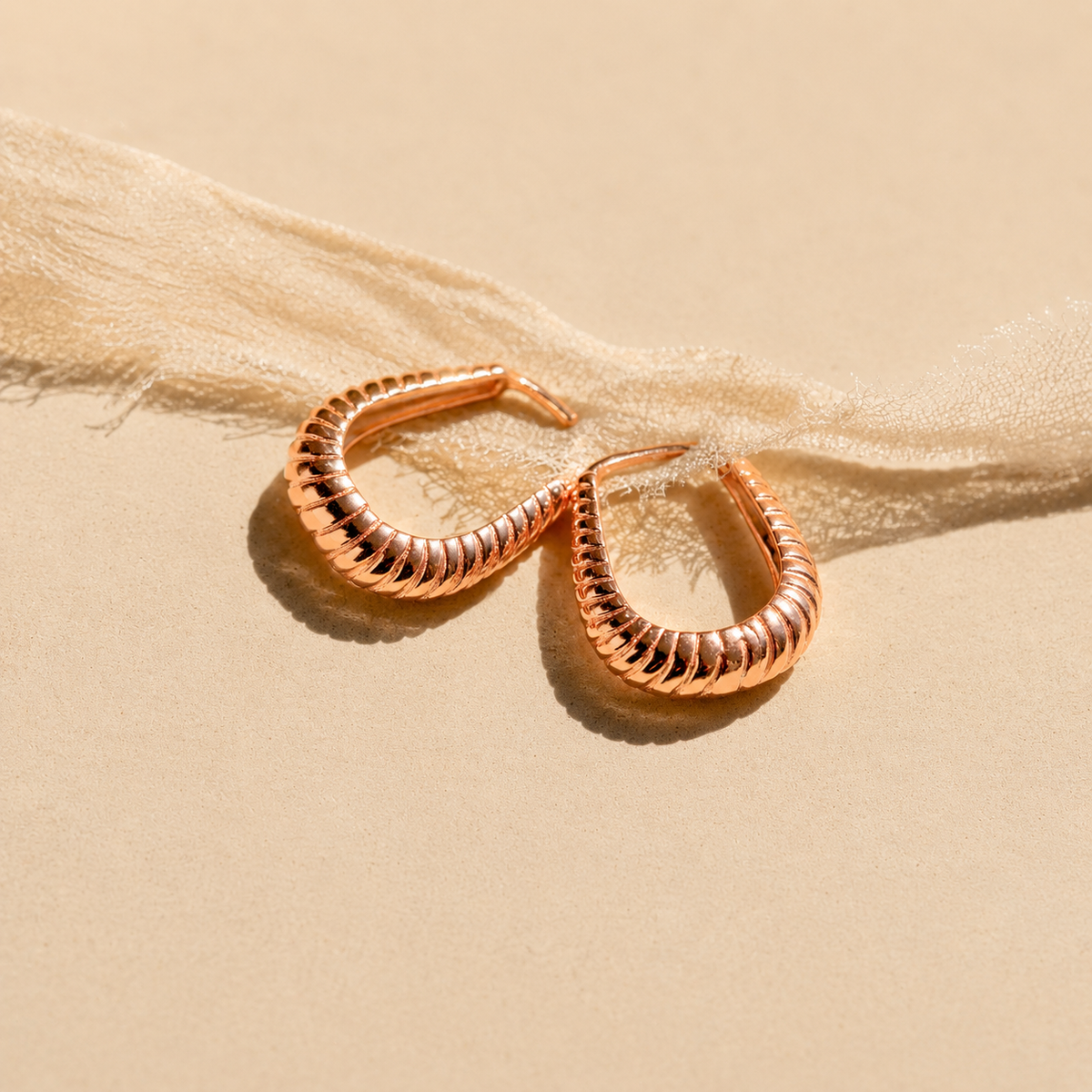 Rose gold hoop earrings on a beige fabric background