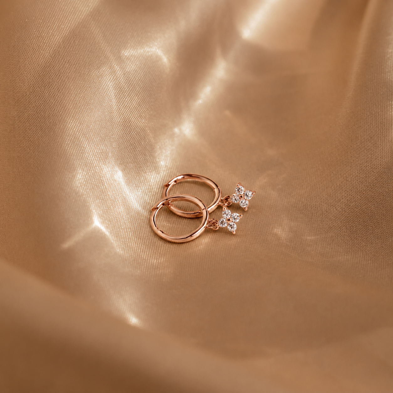 Rose gold earrings with diamond accents on a gold fabric background