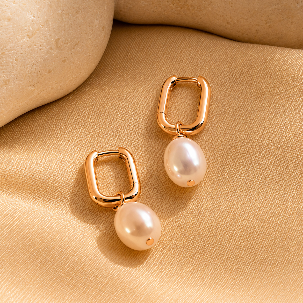 Gold hoop earrings with pearl drops on a beige fabric background