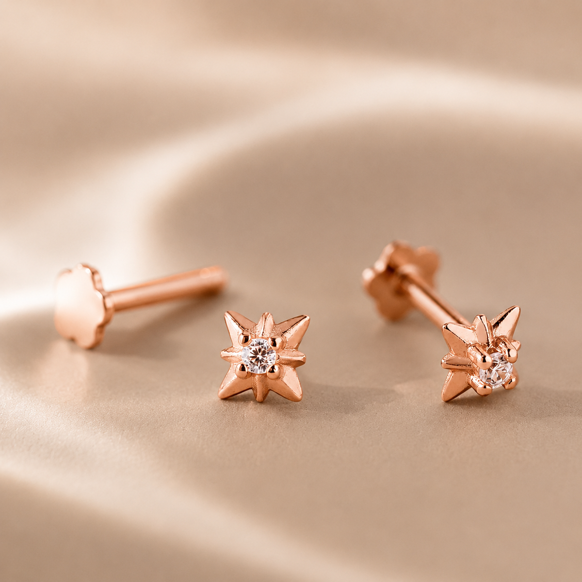 Rose gold star-shaped earrings with a central gemstone on a beige background